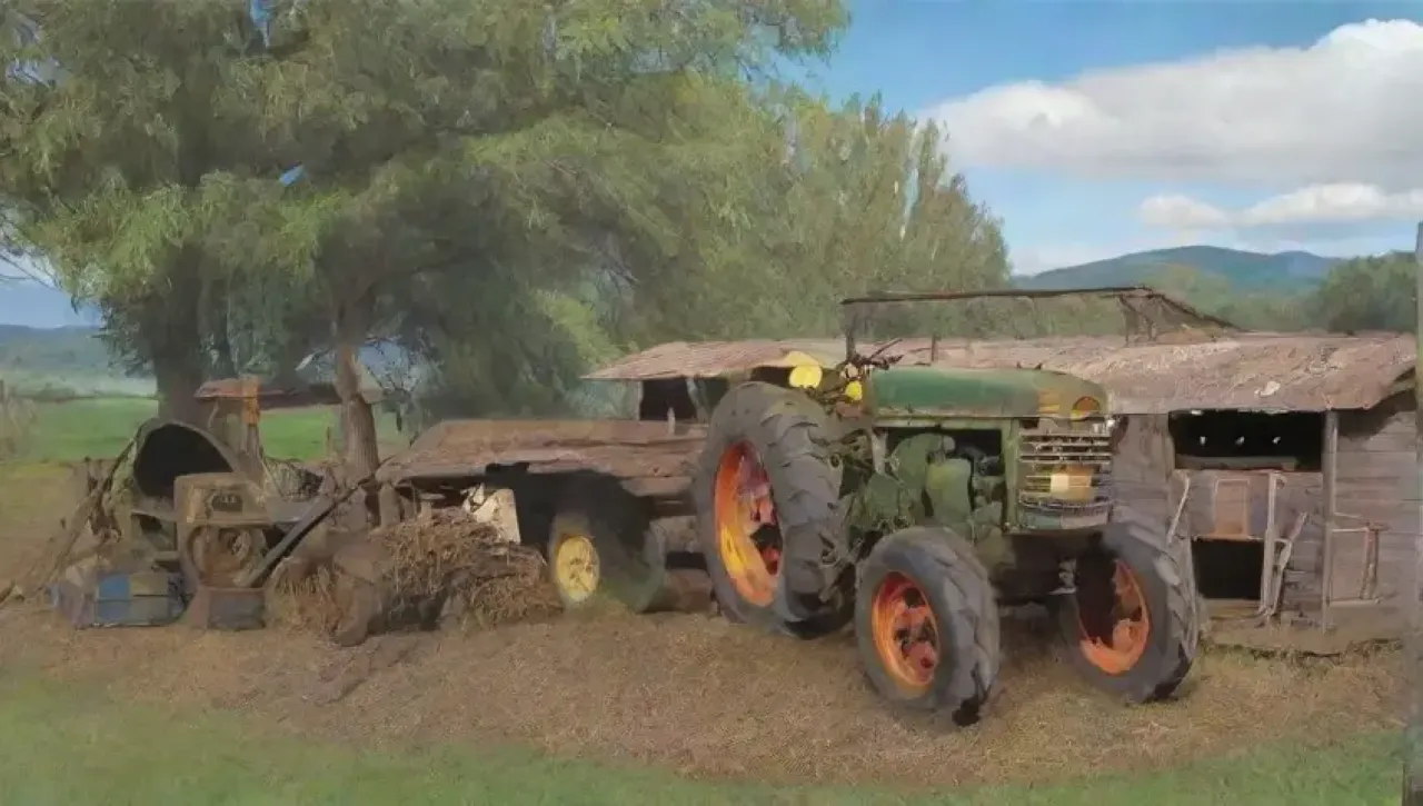 Un viejo tractor verde y desgastado descansa en un campo polvoriento, rodeado de herramientas y un granero deteriorado bajo un cielo azul